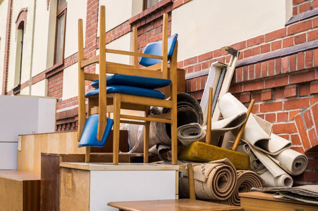 Ein Haufen ausrangierter Möbel und Teppiche vor einem Gebäude, bereit zur Entrümpelung.