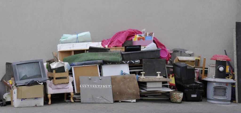 Eine Vielzahl alter Möbel, Elektrogeräte und Haushaltsgegenstände stapeln sich auf einem Gehweg, Teil einer Entrümpelung in Mönchengladbach.