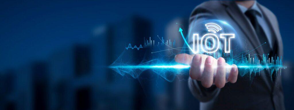  Ein Geschäftsmann hält ein holografisches "IoT"-Symbol in seiner Hand, umgeben von digitalen Grafiken und Diagrammen, die die Bedeutung von Sensoren und Vernetzung im Internet der Dinge darstellen.