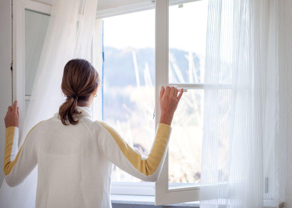 Eine Frau steht an einem Fenster und lüftet