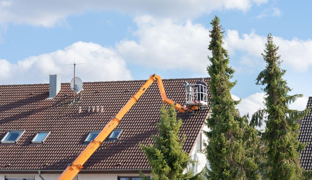 Arbeiter auf Gelenk Teleskop Arbeitsbühne bei Wartungsarbeiten am steilen Hausdach – ideal für schwer zugängliche Stellen in großer Höhe