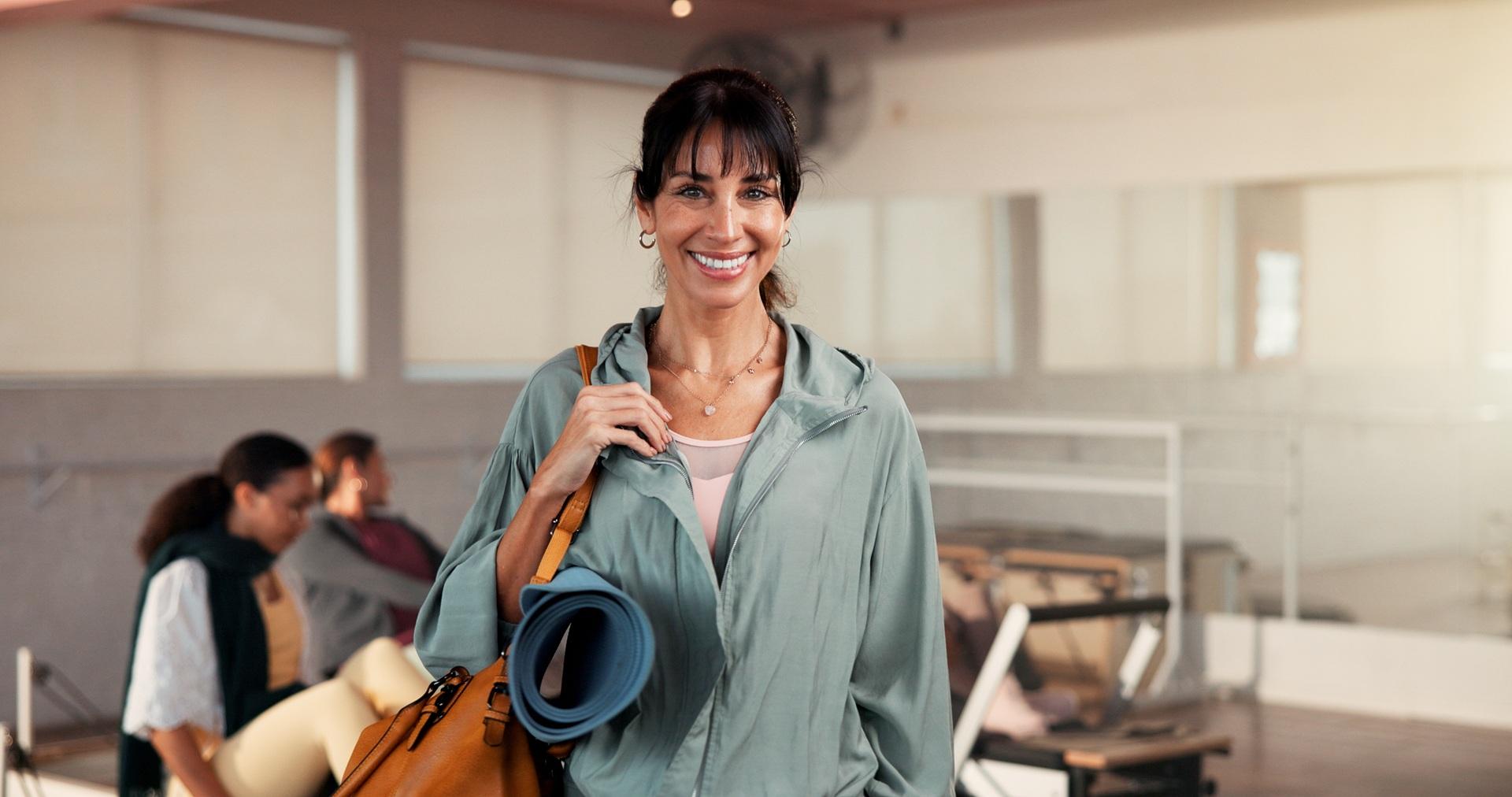 Lächelnde Frau trägt Yogamatte im Studio