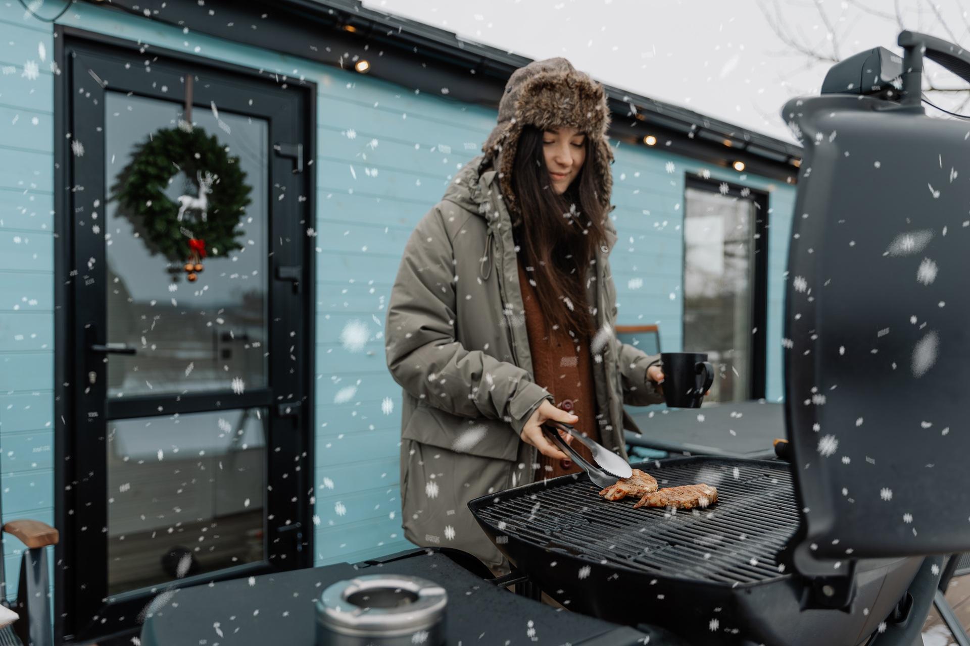 Frau grillt bei Schneefall im Winter | Schwenkgrill kaufen
